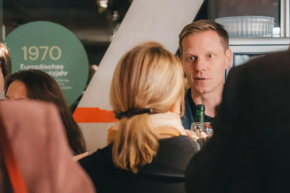 Kai Niebert in Diskussion mit einer Teilnehmerin, im Hintergrund, die DNR-Ausstellung mit dem Element für das Jahr 1970 zum Europäischen Naturschutzjahr